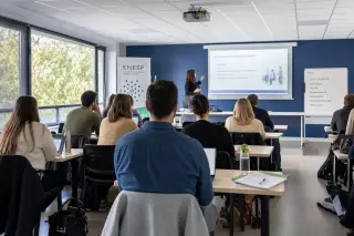 Modern lecture hall with adult students in a professional training session, no identifiable faces, neutral institutional colors and natural daylight.