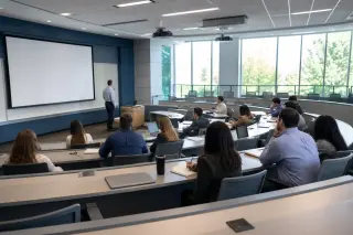 Modern amphitheater during a training session with professionals seated, taking notes, facing a lecturer; neutral-colored, well-lit, professional setting without visible faces.