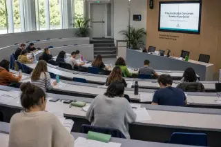 Modern training amphitheater during a morning session, adult students spaced apart focusing on documents, professional atmosphere with neutral tones and natural light, no recognizable faces